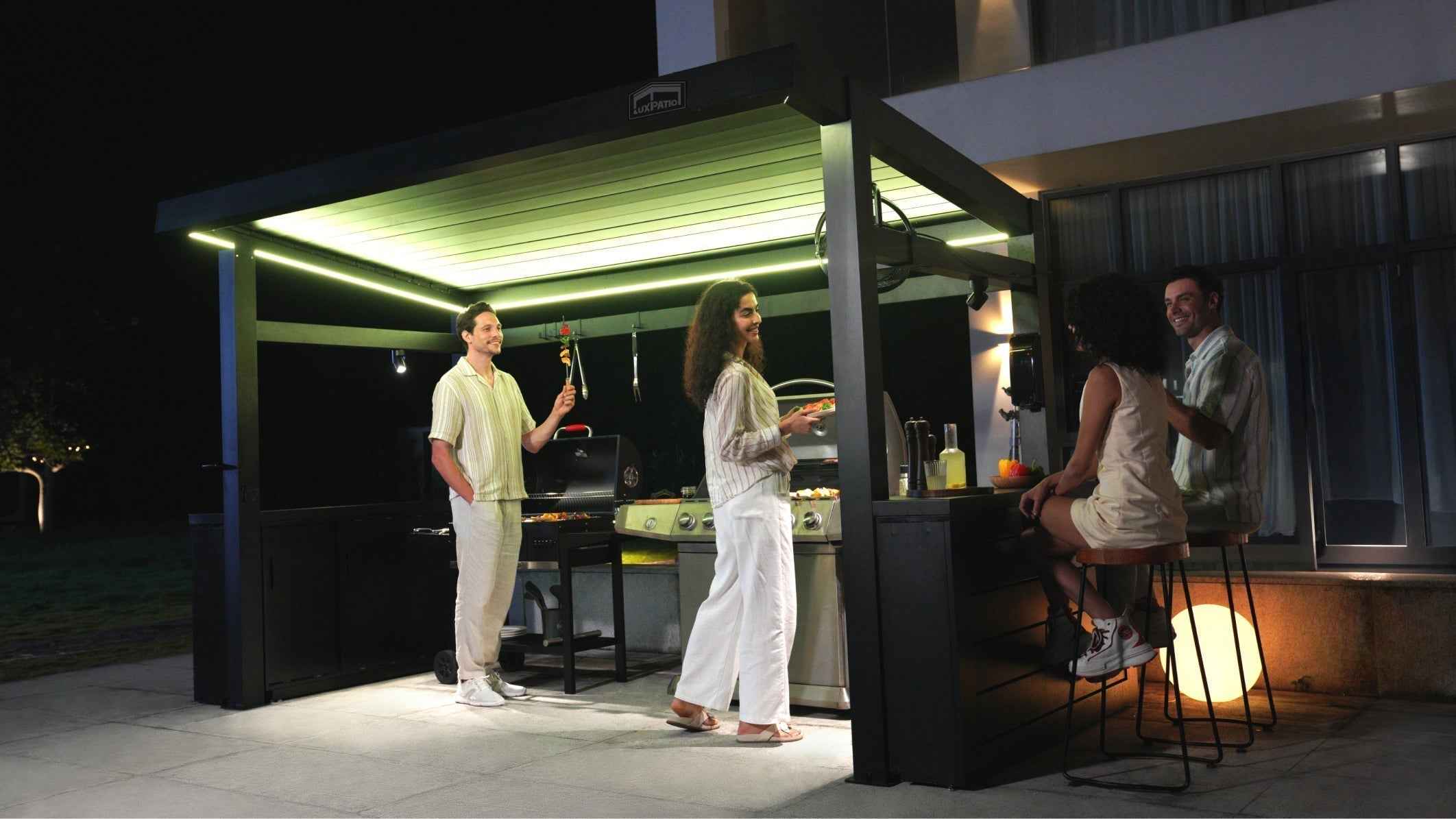 A modern outdoor gathering with warm lighting at the bar and a chat among four people