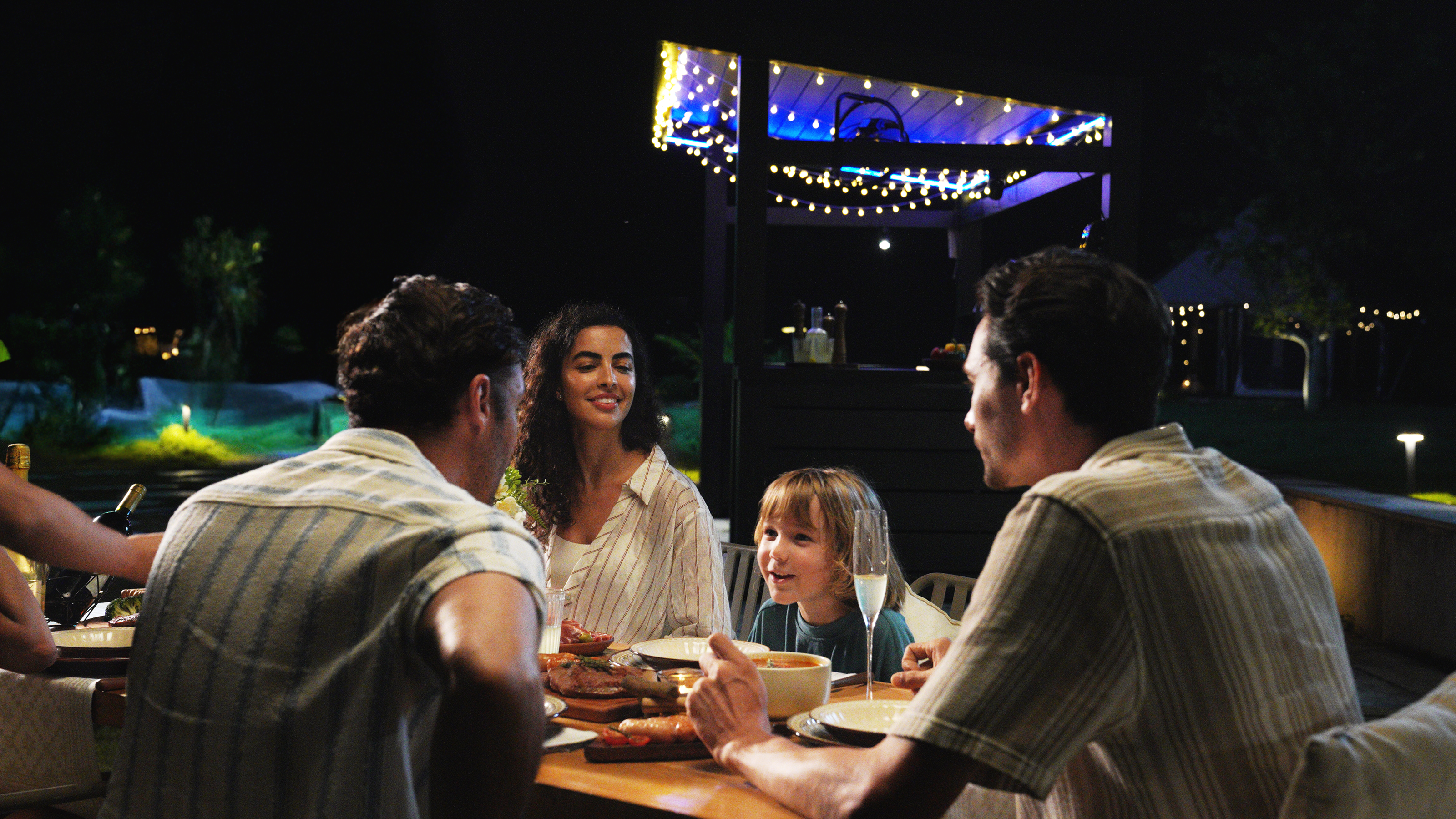 Four people dining outdoors at night under string lights​