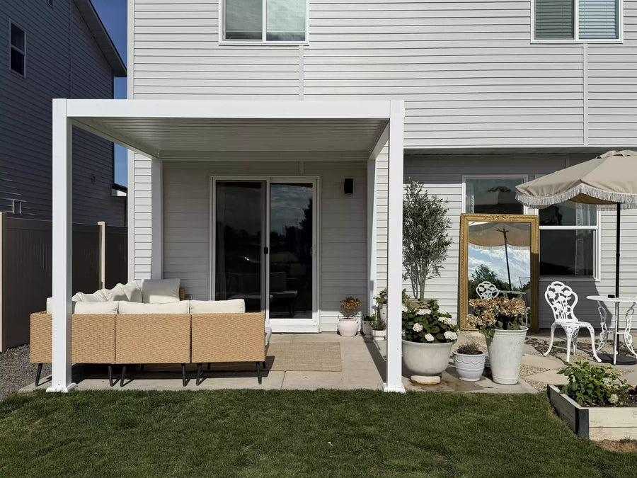 White aluminum pergola installed over a backyard concrete patio outside a suburban home