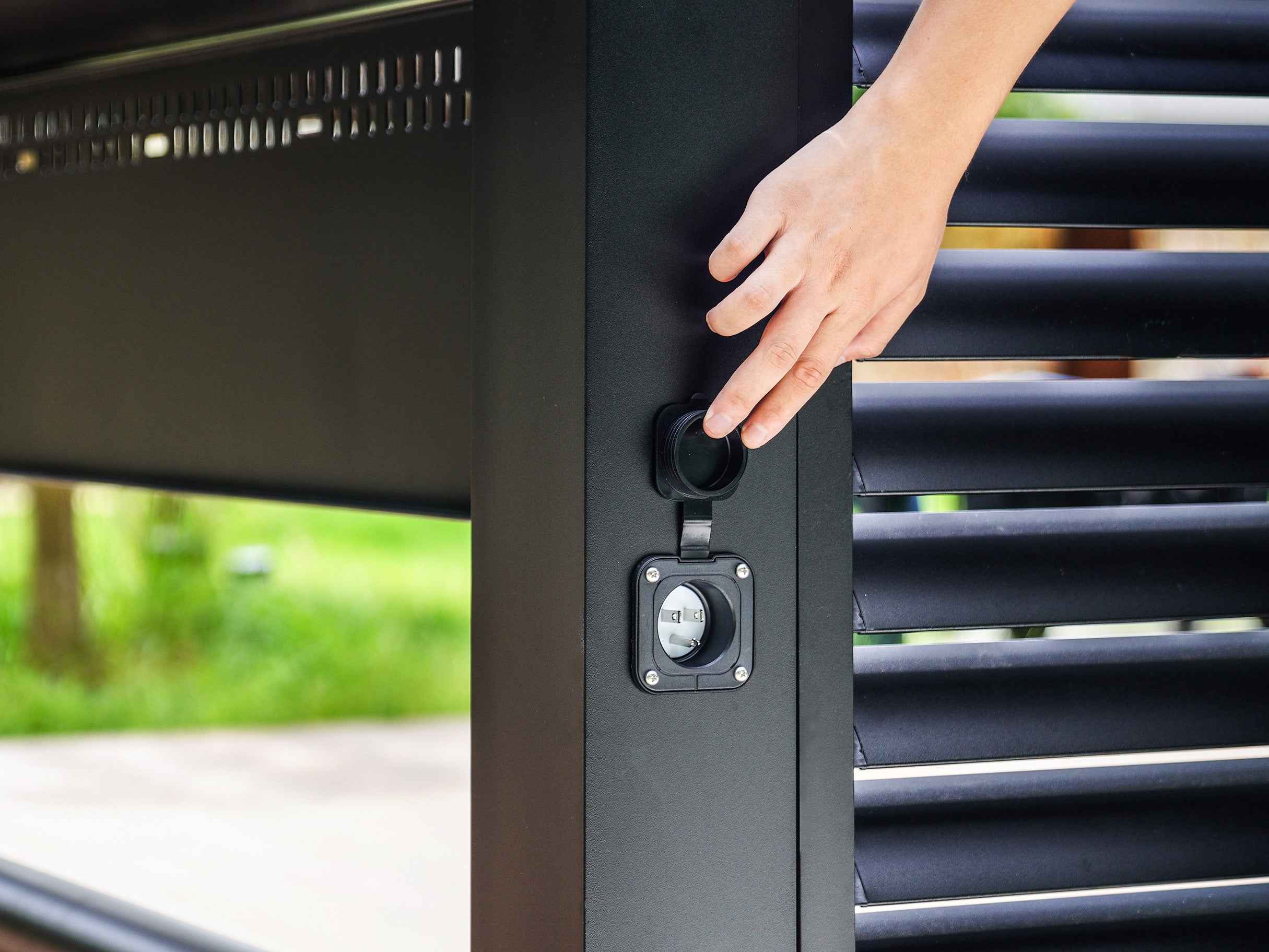 Hand opening weatherproof power outlet cover on Grill Louvered Pergola Pro aluminum construction.